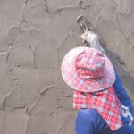 Person applying elastomeric paint on a stucco wall