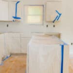 Kitchen cabinets masked off and prepped for painting, showcasing proper preparation techniques.