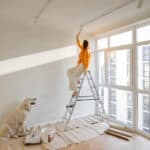 A person painting a large wall with a roller, taking on a big home painting project.