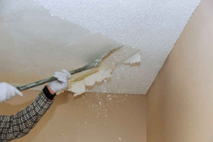 Person in protective gear scraping off old textured ceiling