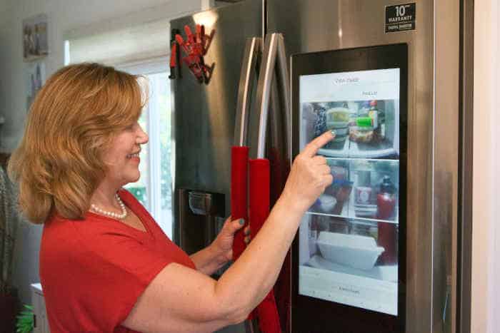 A woman interacting with a touchscreen smart refrigerator in her kitchen.