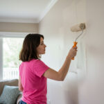 Homeowner attempting DIY interior painting in Ohio living room with roller and uneven wall coverage