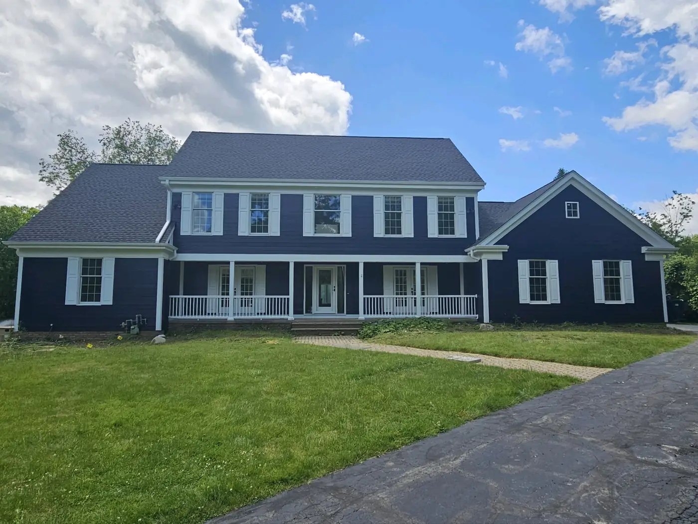 Navy blue two-story craftsman home with white wraparound front porch after exterior house painting by Crocker Home Painting in Westlake, Ohio